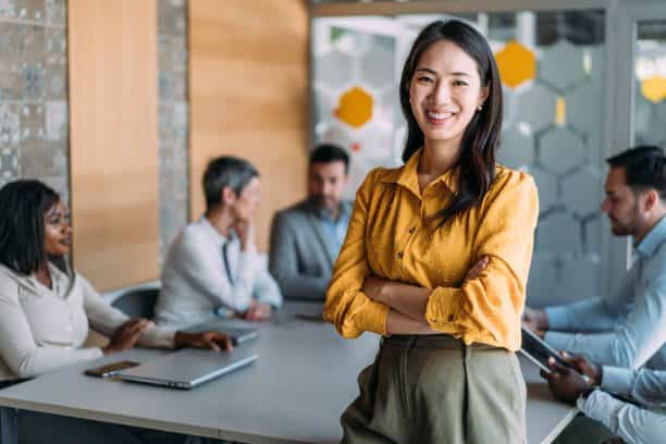 Portrait of beautiful smiling businesswoman with her colleagues on meeting in board room. Successful team leader and her team on a seminar in the office. Shot of confident businesswoman sitting on the conference table with her coworkers working in background.