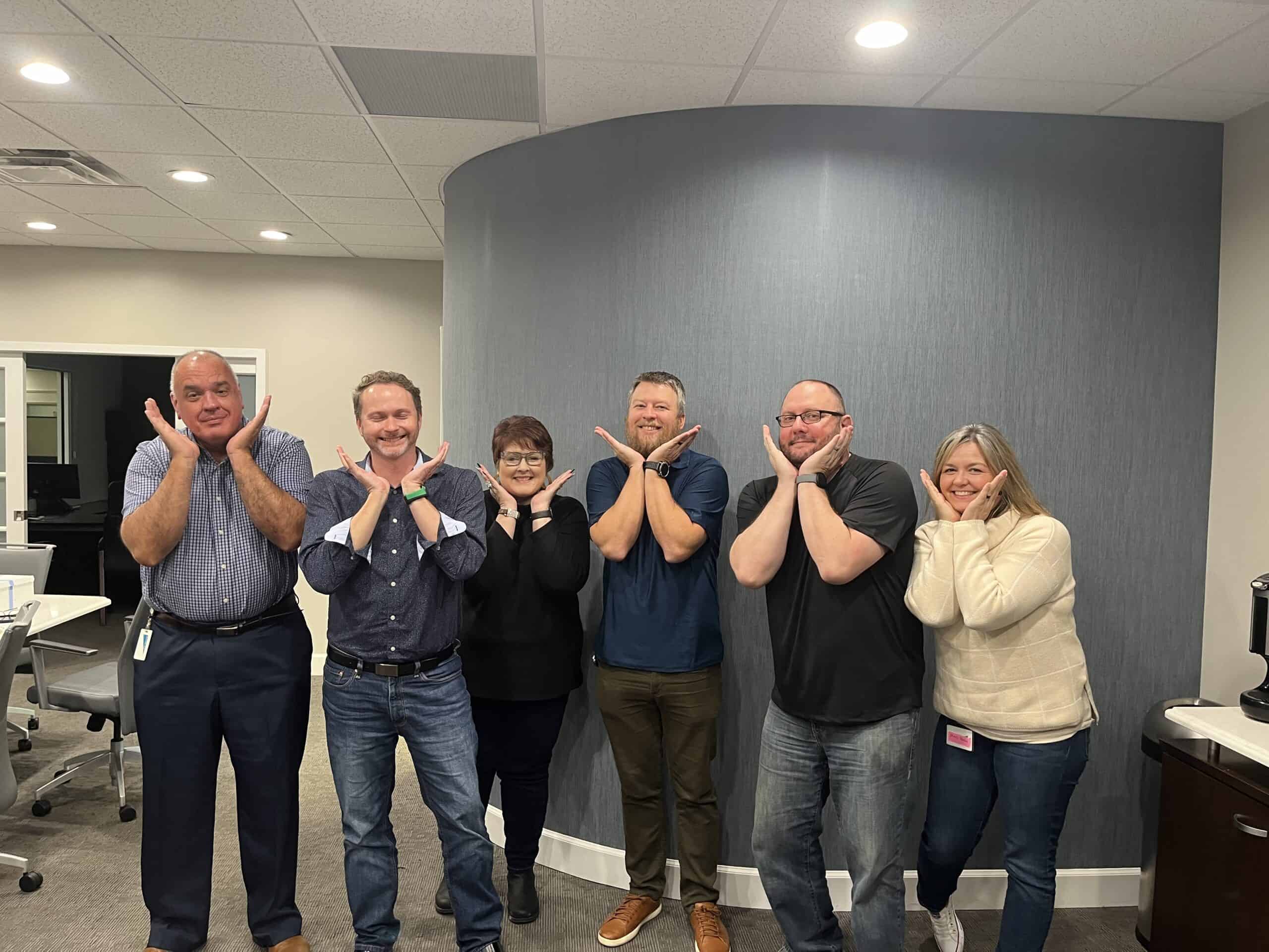 Group of six diverse professionals making playful gestures in office.