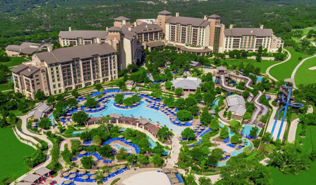 Aerial view of a large resort with pools, greenery, and hotel buildings.