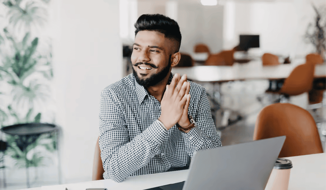 Smiling man in office with laptop, looking confident and professional.