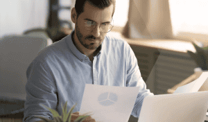 Man analyzing data report with laptop and charts in office.