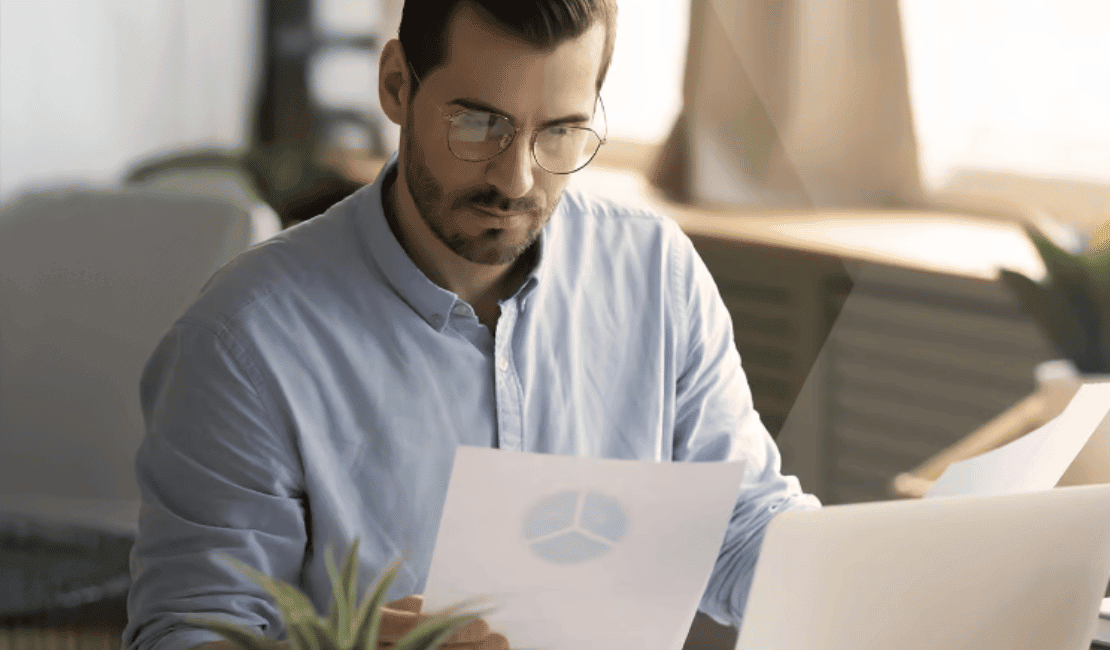 Man analyzing data report with laptop and charts in office.