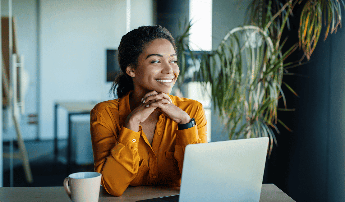 Smiling woman in professional attire working on a laptop in an office setting.