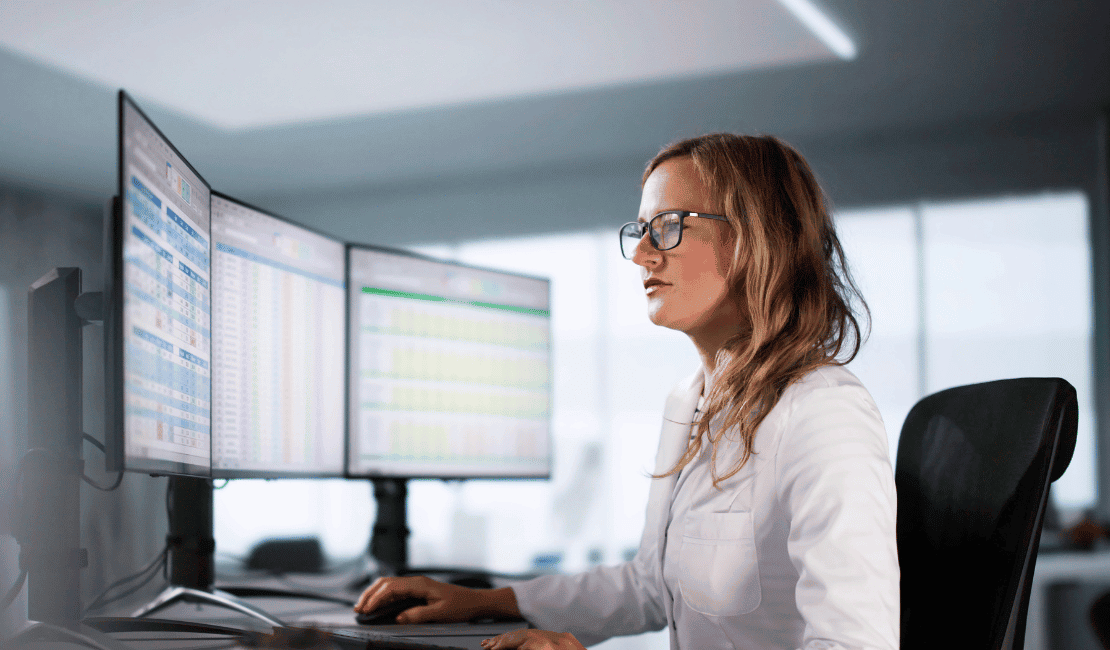 Healthcare professional analyzing data on multiple monitors in an office.